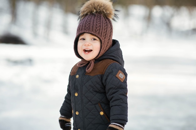 Charming little boy in a funny winter hat poses in the park