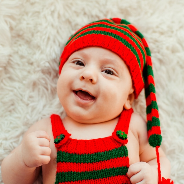 Charming little boy in long green and red hat lies on fluffy carpet 