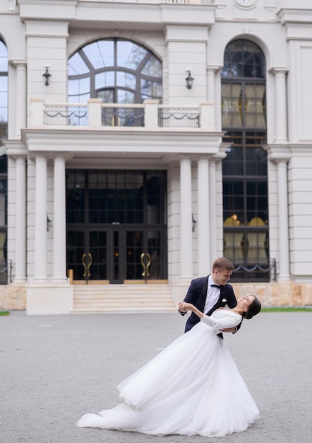 Charming man and woman having first dance outdoors near large restaurant Loving bride couple enjoying of the moment looking at each other Cute bride and groom having fun