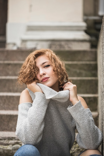 Charming smiling lady holding sweater's collar and sitting on steps