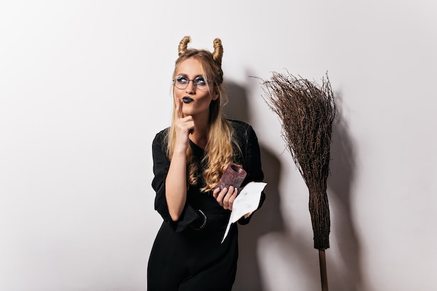 Free Photo charming witch in glasses posing on white wall. indoor photo of pensive vampire girl enjoying halloween party.