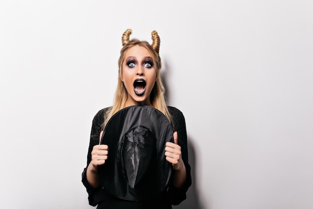 Free photo charming witch posing with surprised face expression. scared caucasian girl celebrating halloween.