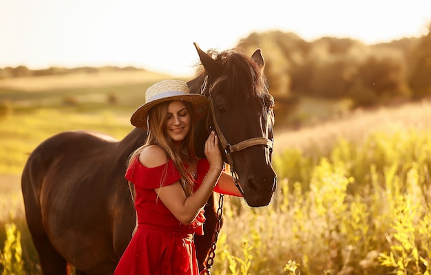 Free photo charming woman in a hay hat and red dress stands with a horse on the green field