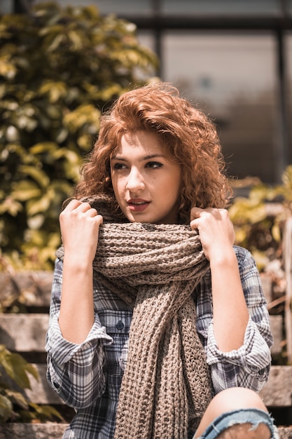 Free photo charming woman sitting on steps and holding scarf