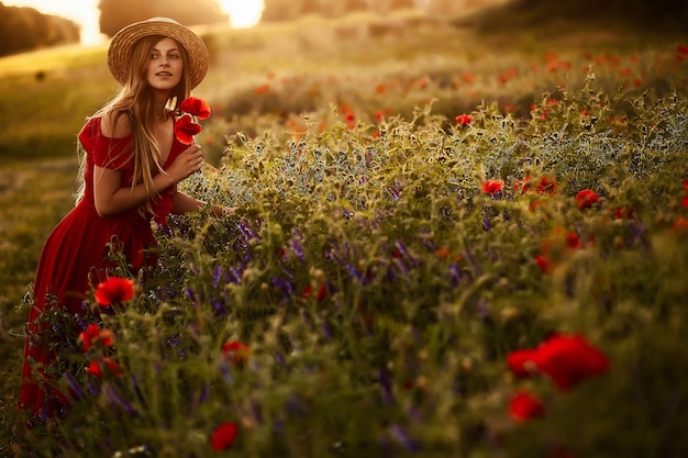 Charming woman walks across a green field with poppies in the rays of evening sun