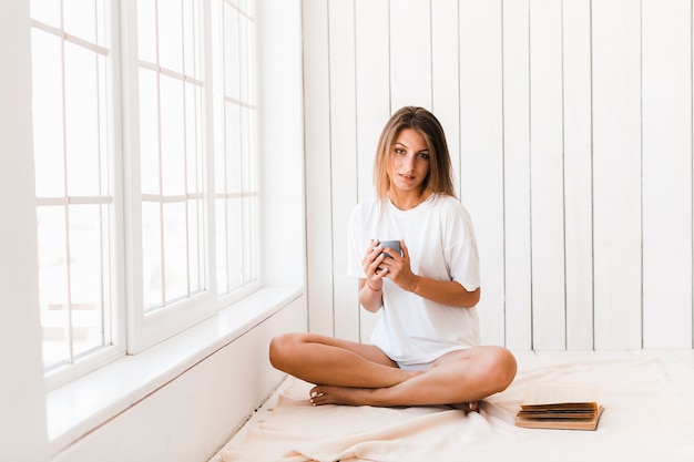 Free photo charming woman with beverage sitting near window