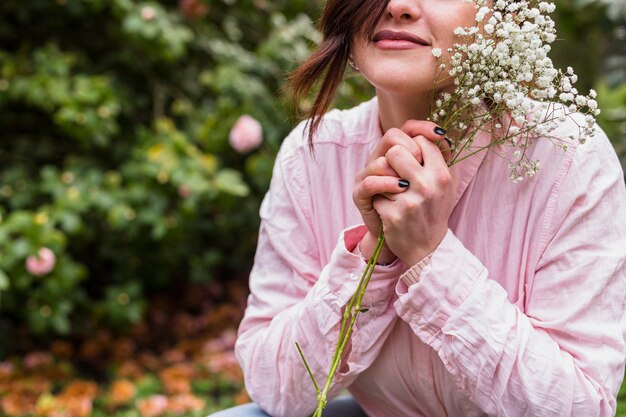 Charming woman with bunch of plant with white blooms near face