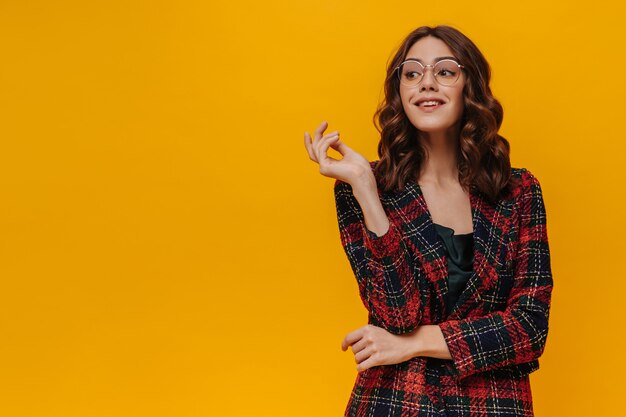 Charming woman with curly hair in eyeglasses posing on isolated wall