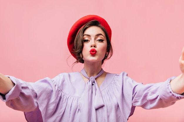 Free photo charming woman with red lips sends kiss. lady in beret makes selfie on pink background.