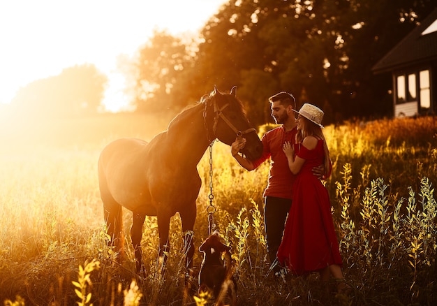 Charming young couple stands with a brown horse before a country house