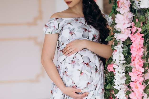 Free Photo charming young pregnant woman poses in a studio with pink flowers