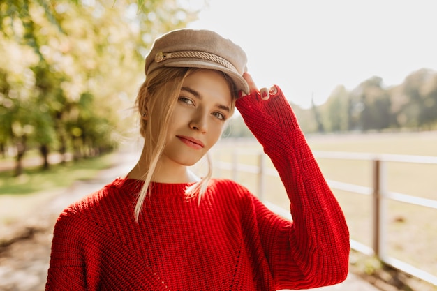 Free Photo charming young woman in red pullover and light hat looking good in the park. beautiful blonde wearing nice accessories and trendy clothes in the autumn.