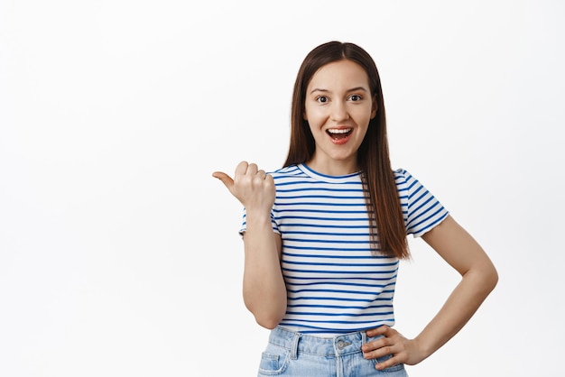 Check out this sale Impressed young woman share info pointing finger left at news event banner advertisement smiling satisfied making announcement white background