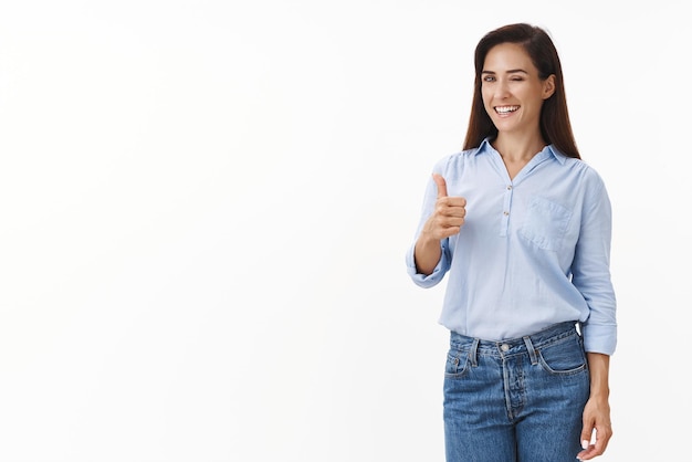 Cheeky confident businesswoman aim success win deal wink sassy smiling pleased show thumb up gesture grin positive judgement like your idea stand white background give approval