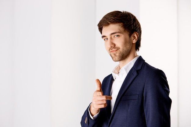 Free photo cheeky confident handsome young businessman, pointing finger and smiling, praising you making good work