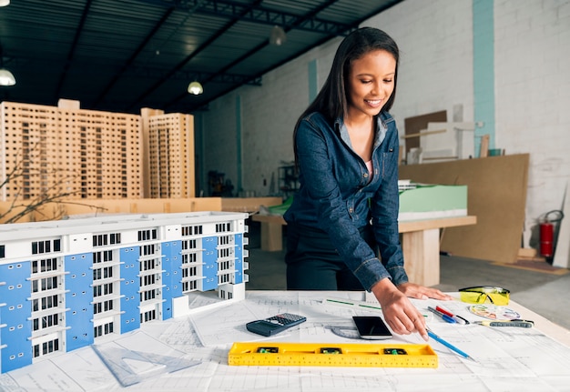 Free Photo cheerful african-american lady standing near model of building on table