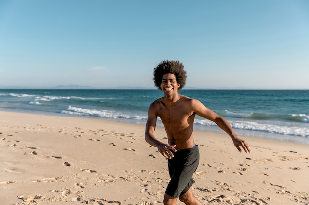 Cheerful African American male running on seashore