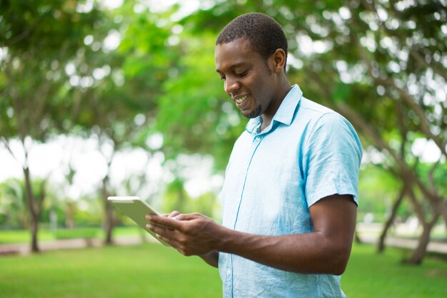 Cheerful African-American man using tablet to interact on social media.