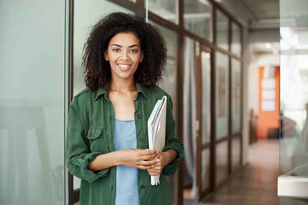 Cheerful african beautiful woman student smiling holding books in university. Education concept.