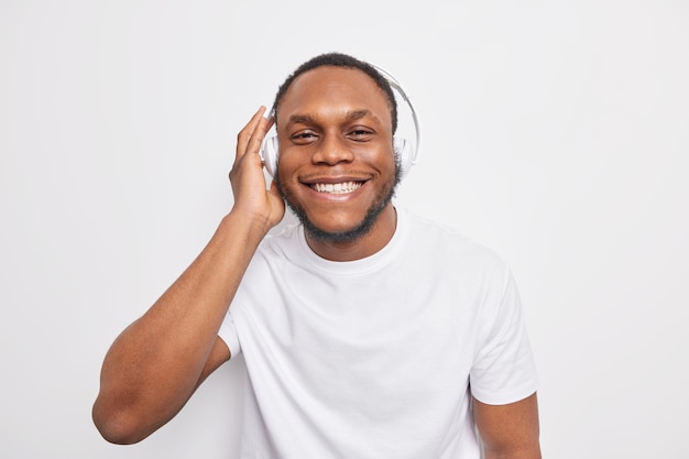 Cheerful Afro American guy listens to  favorite music via headphones smiles happily 