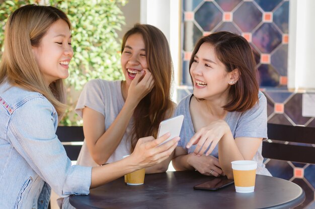 Cheerful asian young women sitting in cafe drinking coffee with friends and talking together