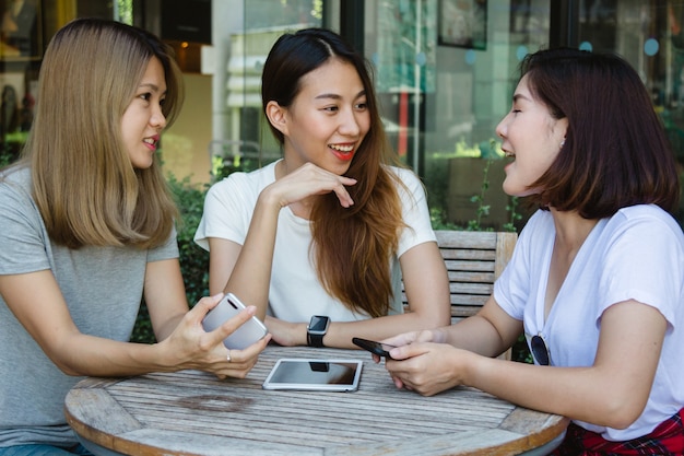 Cheerful asian young women sitting in cafe drinking coffee with friends and talking together