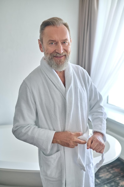 Cheerful attractive gentleman belting his terry bathrobe