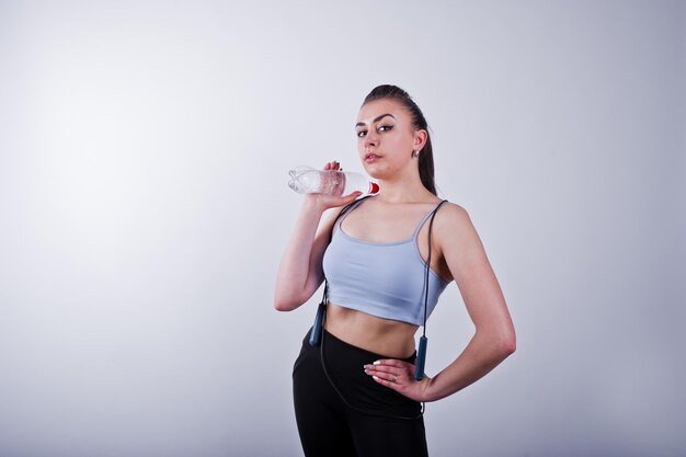 Cheerful attractive young fitness woman in top and black leggings with jump rope and bottle of water isolated over white background