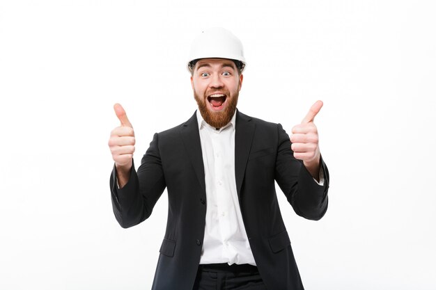 Cheerful bearded business man in protective helmet showing thumbs up