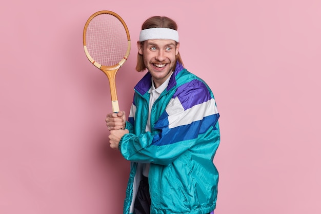 Free photo cheerful bearded man player holds tennis racket enjoys active game on court dressed in activewear has happy expression looks into distance.