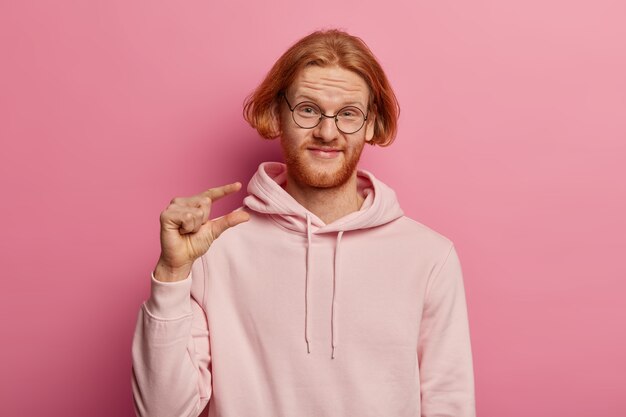 Cheerful bearded man with stylish hairdo, ginger beard, gestures little object