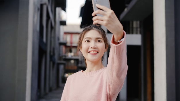 Cheerful beautiful young Asian backpacker blogger woman using smartphone taking selfie while traveling at Chinatown in Beijing, China. 