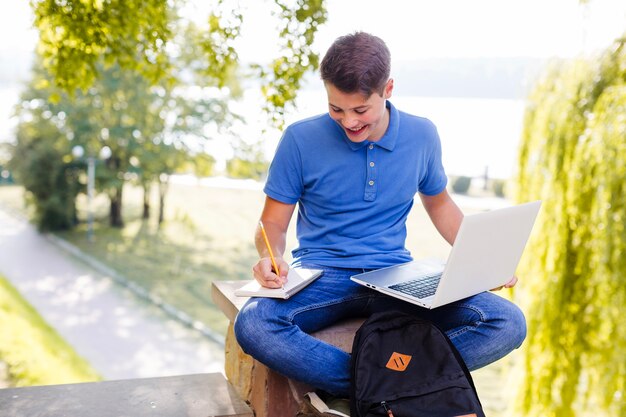 Cheerful boy doing homework in park