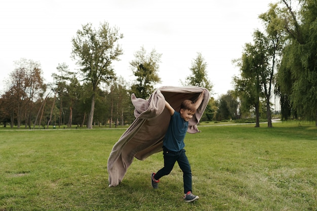 Cheerful boy running with a flying blanket in the park