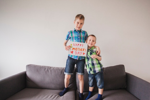 Free photo cheerful brothers with sign to celebrate mother's day