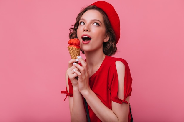 Free photo cheerful brunette girl in red t-shirt posing with ice cream. indoor photo of winsome lady in beret eating dessert.