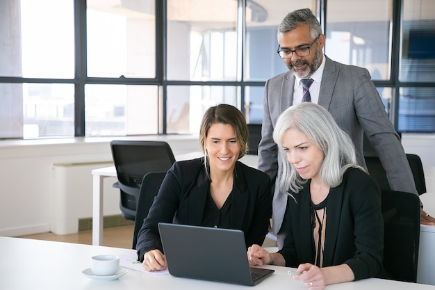 Cheerful business team watching presentation on laptop, sitting at workplace, staring at display and smiling. Copy space. Business meeting concept