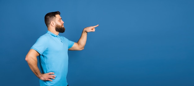 Cheerful. Caucasian beautiful man's portrait isolated on blue  wall with copyspace. Male model with beard.