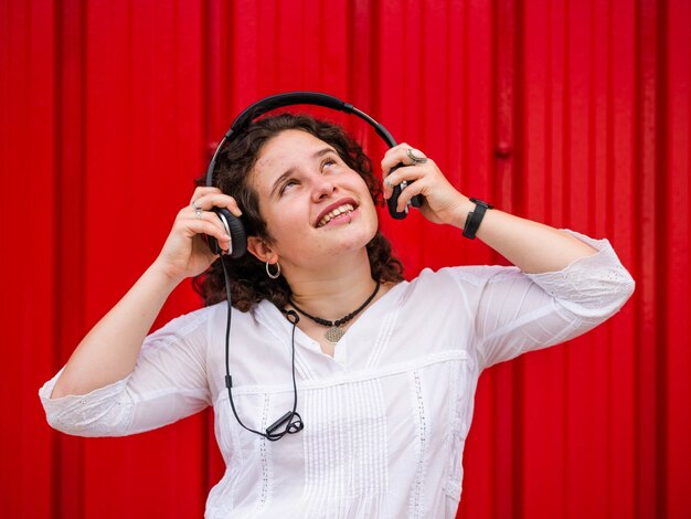 Cheerful Caucasian female listening to music with headphones on red background