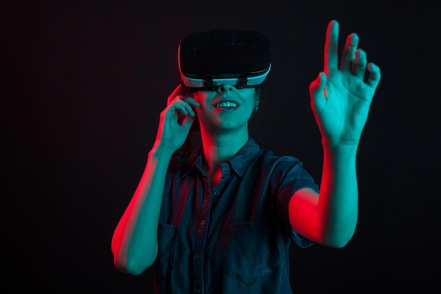 Cheerful caucasian woman enjoying herself with virtual reality helmet in studio. Futuristic goggles for virtual reality used by beautiful woman.