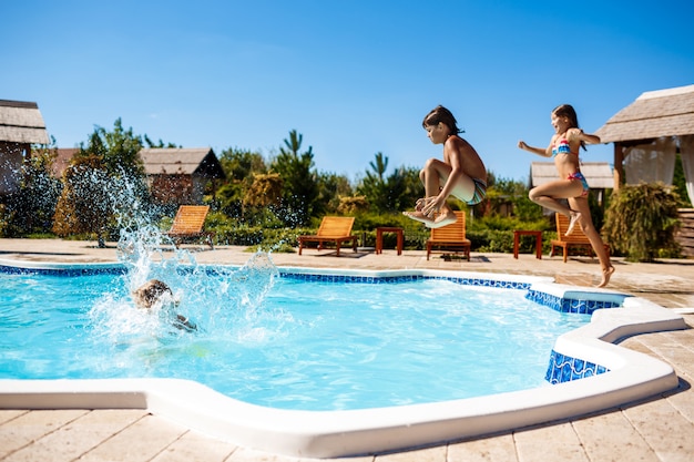 Cheerful children rejoicing, jumping, swimming in pool.