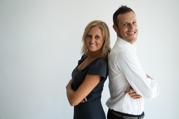 Cheerful confident business couple standing back to back and looking at camera