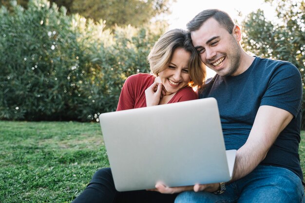 Cheerful couple browsing laptop on ground