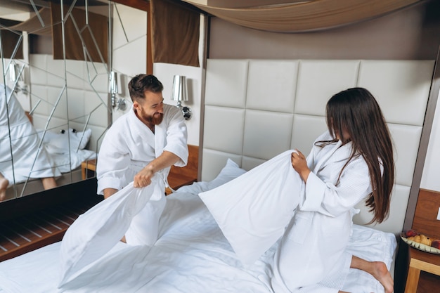 Cheerful couple have fun in the bedroom fighting with big pillows at home