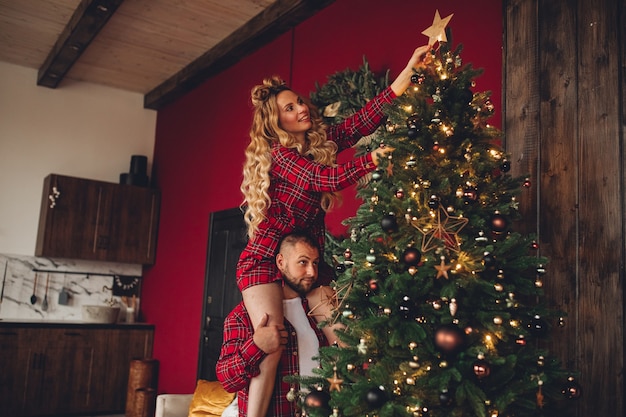 Cheerful couple in love in the same sleepwear decorates christmas tree together at home