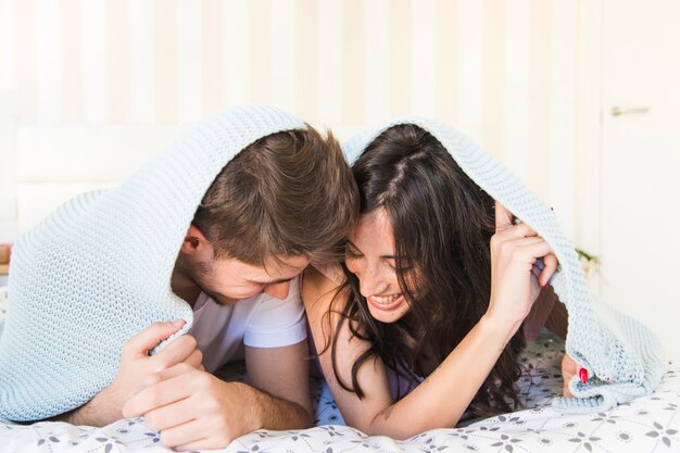 Cheerful couple lying under blanket