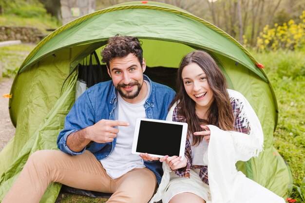 Cheerful couple near tent pointing at tablet