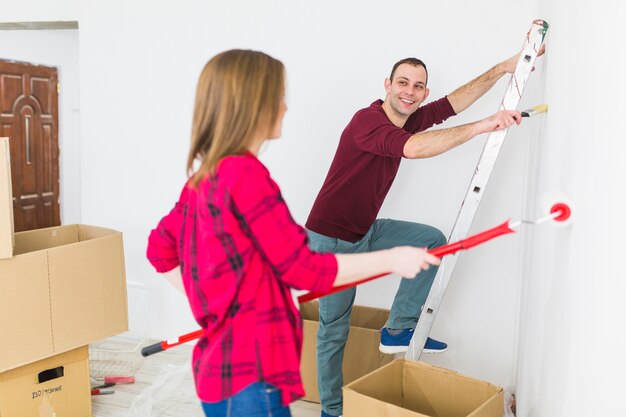 Cheerful couple painting walls in apartment