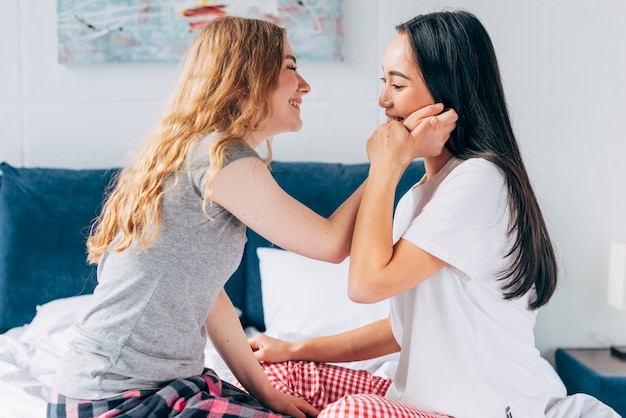 Cheerful couple sitting in bed and touching face