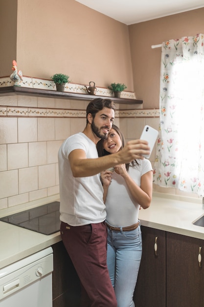 Cheerful couple taking selfie in kitchen